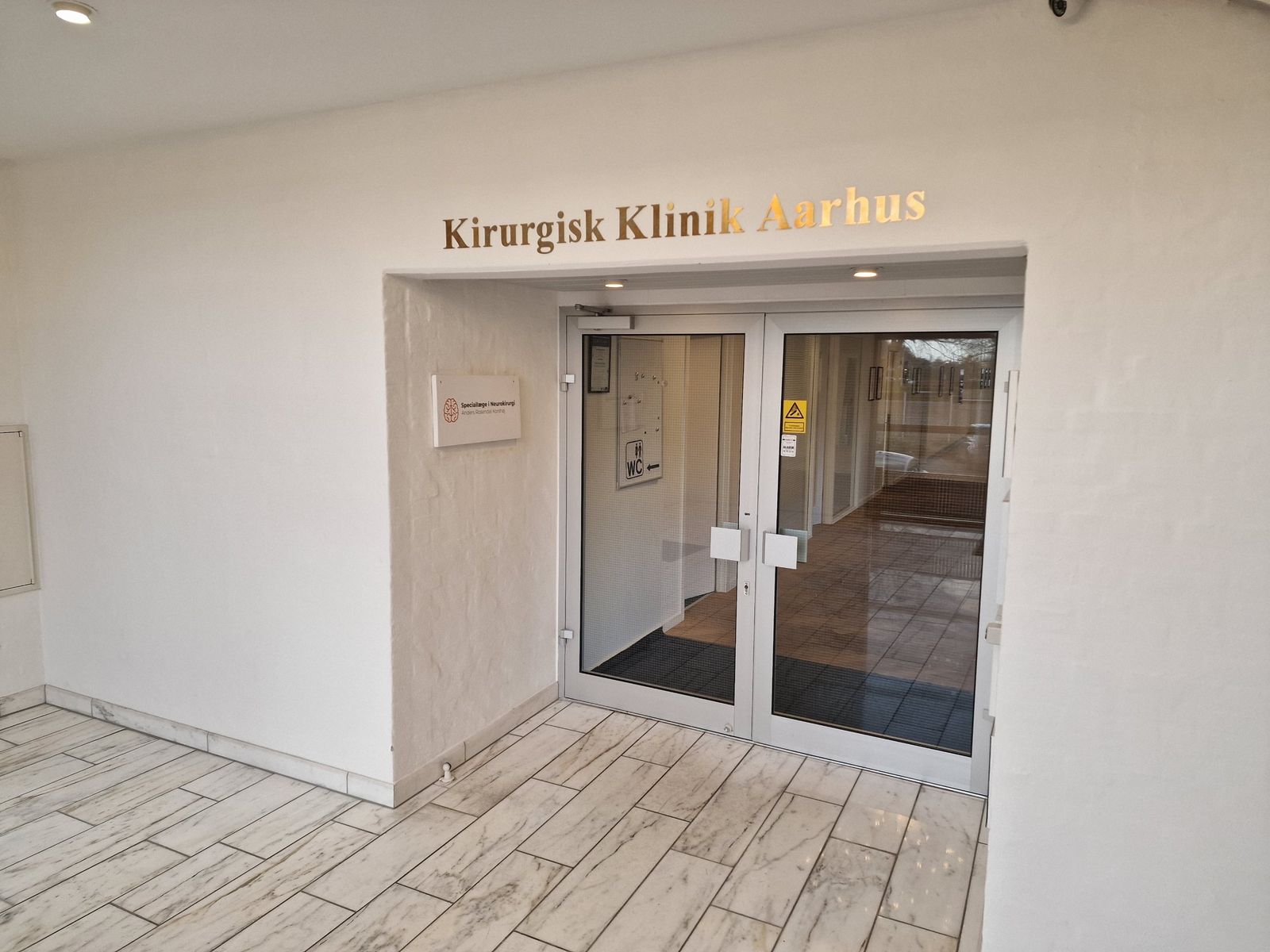 Glasdøren ind til klinikken med navnet Kirurgisk Klinik Aarhus over døren